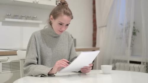 Excited Woman Reviews Documents at Kitchen Table
