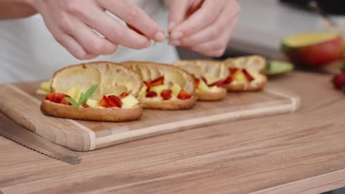The woman is preparing pastries and she decorates them with mint leaves on top of the filling