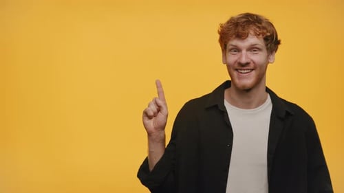 Smiling Young Man Pointing Left on Yellow Background