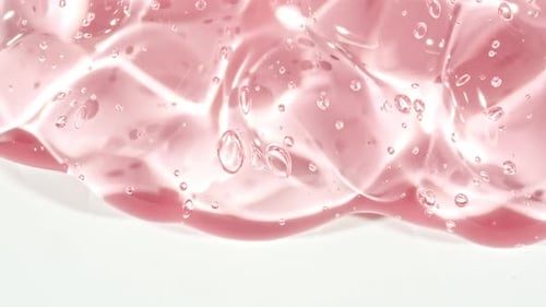 Gel cosmétique fluide rose transparent avec des bulles de molécules coulant sur la surface blanche