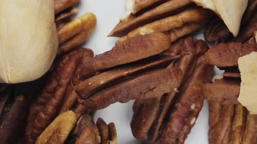 Peeled pecans spin against the background of other nuts. Close-up. View from above.