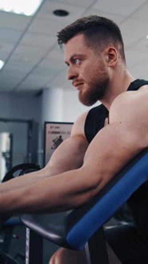 Bearded man pumping his arm muscles in the gym.