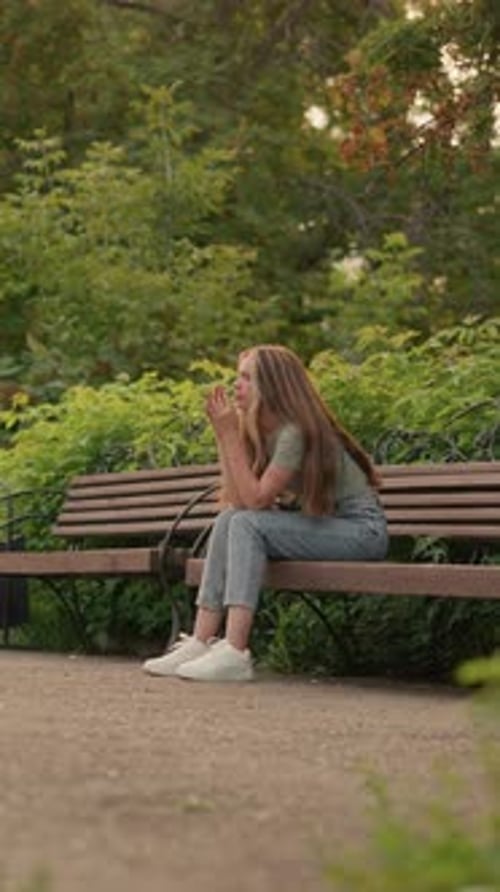 Reflective Woman Sitting on Park Bench Surrounded By Greenery in Peaceful Setting