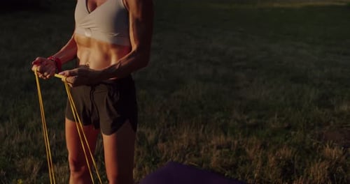 Woman Exercises in a Grassy Field with Bands