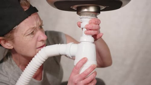 Plumber repairing water leak under sink.