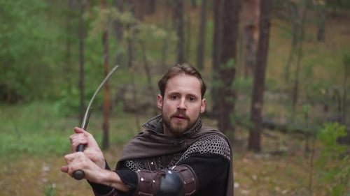 Strong Knight with Mail and Cape Strikes By Sword in Forest