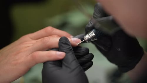Beautician in Black Gloves Carefully Using Electric Nail Drill to Treat Male Client Cuticles in