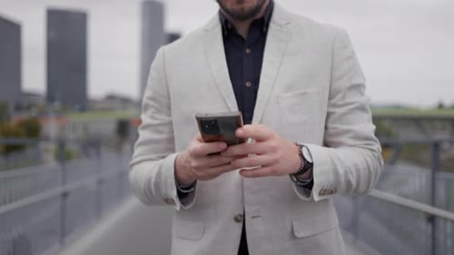 Gros plan de l'homme d'affaires inconnu envoyant un texto sur un téléphone portable en traversant le pont.
Y