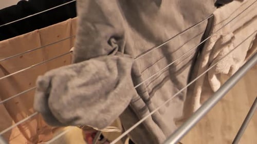 Hands Putting Clothes on a Drying Rack Indoors