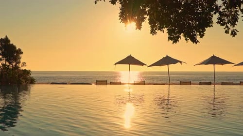Seascape shot from a tropical resort with swimming pool and umbrellas in the foreground and golden s