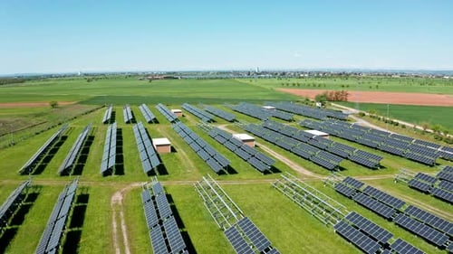 A solar farm in a vast green field on a sunny day, aerial view