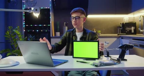 Beautiful Smiling Teen Boy in Glasses Holding a Green Screen Tablet while Chatting Online with Frend