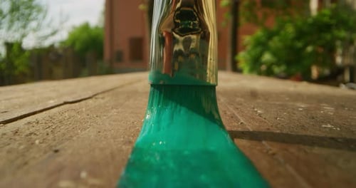 Alternative angle shot of a painting brush is coloring a wooden table with green color outdoor in