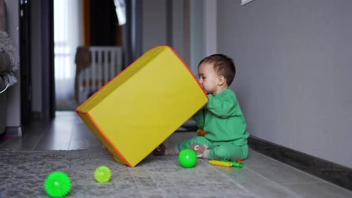 Adorable baby reaches to get a big yellow toy box. Lovely kid wants to take the toys from box.