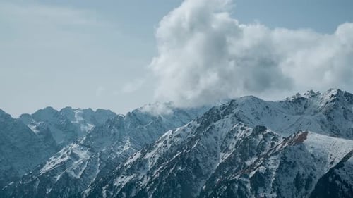 Clouds Forming Over Rocky and Snowy Mountains