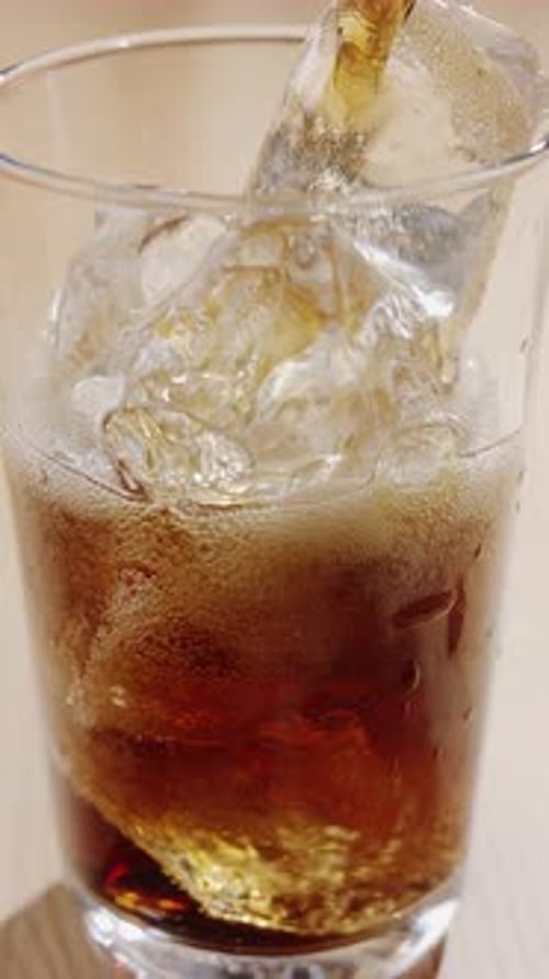 Close-up shot of cola being poured into a glass on the table with visible foam.