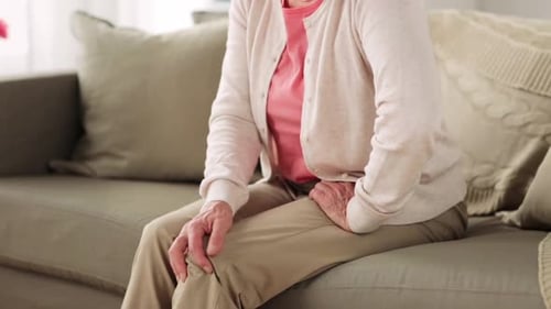 Senior Woman Massaging Knee Sitting on Couch