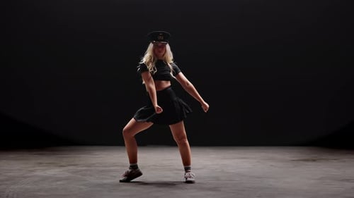 Junge Frau mit Polizistenhut tanzt im Studio vor schwarzem Hintergrund