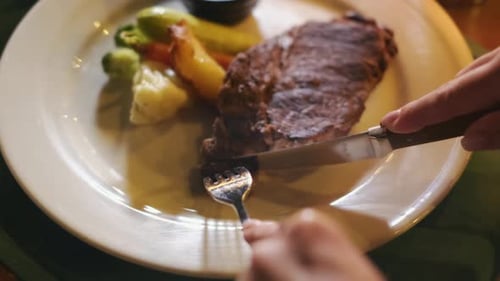 Close-up partial view of woman eating steak with fork and knife. 4K. a nutritious meal serving.