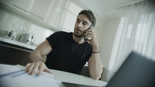 Man Talking on Phone at Table with Laptop
