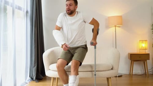Injured Man Standing With a Crutch in His Home