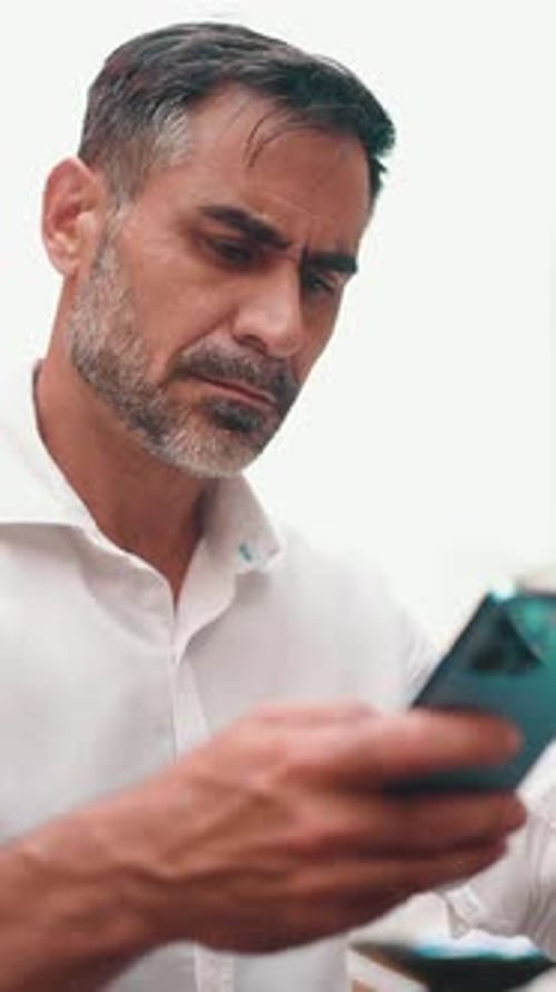 Mature businessman sitting at cafe table, drinking coffee and typing on smartphone