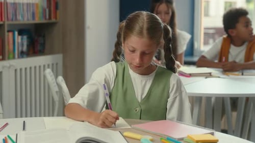 Focused Girl Writing in School Classroom with Students
