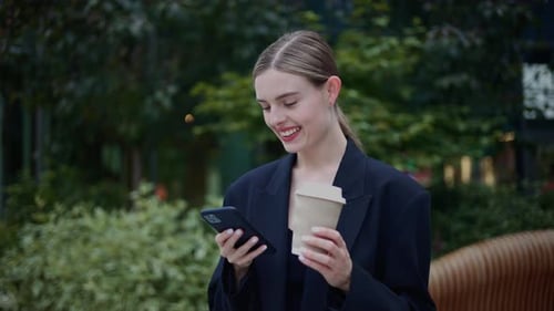 Smiling Woman Using Phone with Coffee Outdoors