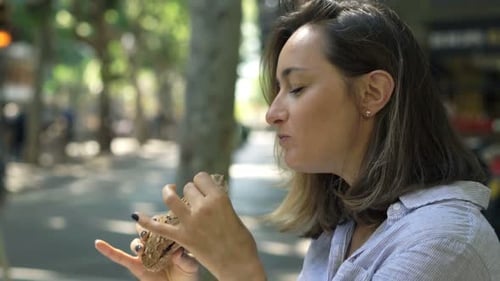 Young woman enjoying a delicious sandwich on a bench in the city
