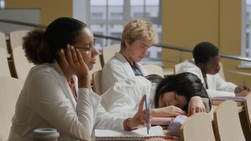 Black Female Medical Student Sitting at Desk with Tired Group in Lecture Class