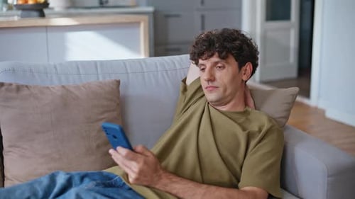 Young Man Relaxing on Sofa with Smartphone