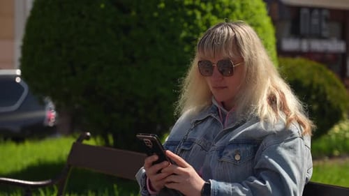 Woman Using Smartphone on Park Bench in City