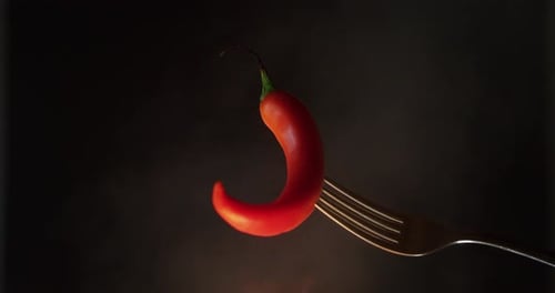 Close up of a red chili pepper holded by a fork with the fire in the background. Concept: Chili, s