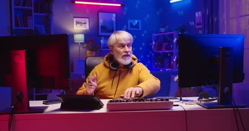 Joyful Pensioner Caucasian Senior Man DJ Sitting at Desk in Room Playing Music at Home Studio in