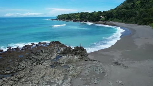 Drone view of beautiful blond girl in sexy swimwear standing on cliffs at a paradise beach in Costa