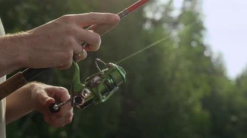 Male Hands Spinning Reel on Fishing Rod Close Up