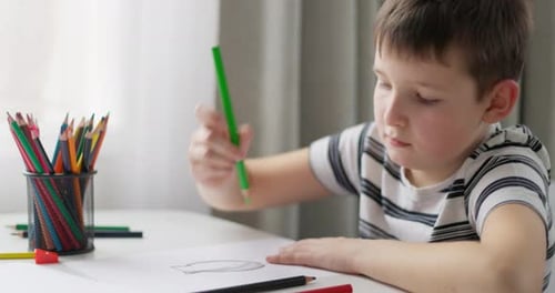 Ein Junge zeichnet mit Buntstiften auf weißem Papier, während er an einem Tisch sitzt