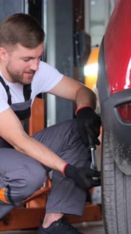 Man with Strong Muscles Changing Automotive Tire on Red Vehicle in Garage
