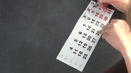 Hand Crossing Out Days on a Calendar Page with a Black Felt Pen