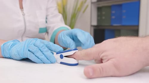 Doctor using pulse oximeter measures oxygen level in blood of man in medical office