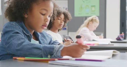 Video of biracial schoolgirl sitting at desk writing in diverse school class