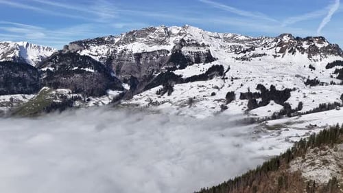 snow layered swiss ridges rise above drifting valley clouds under a clear blue sky