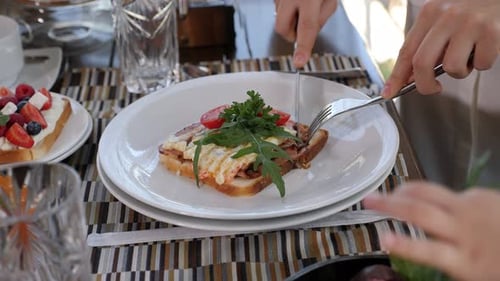 Closeup of a Woman Cutting an Egg and Bacon Sandwich with a Knife in a Cafe