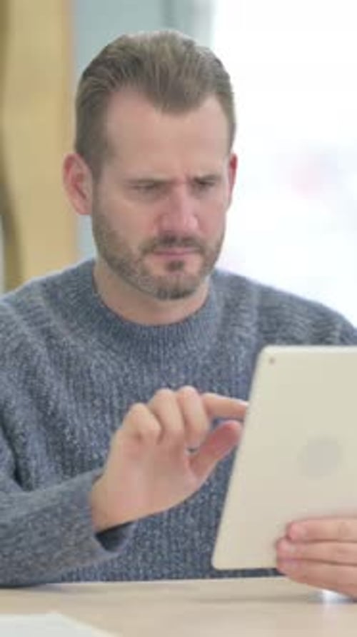 Man with Tablet Displaying Sadness and Frustration Indoors