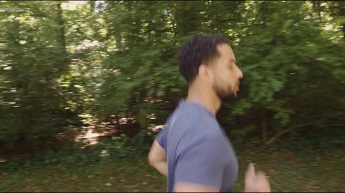 Man Jogging Through Lush Forest on Sunny Day