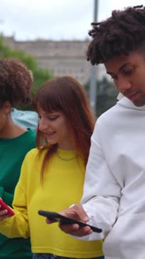 Three Young Adults Looking at Phones in the City