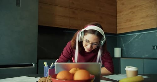 Woman Writes at Table While Looking at Tablet
