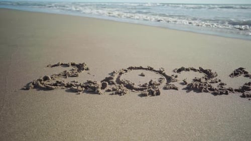 Year 2021 written in the sand at the beach is partially getting washed away by a sea wave