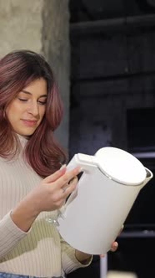 Vertical Video Girl with Beautiful Hair Examines a White Electric Kettle in a Home Appliance Store