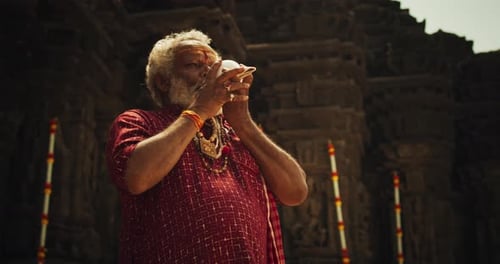 Photo authentique d'un moine indien âgé soufflant une conque dans un ancien temple en pierre. Personnes âgées